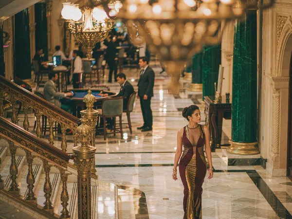 sportsbet.io + Woman in a maroon and gold dress in a chandelier-lit casino lobby