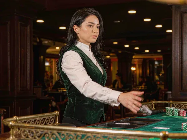 sportsbet.io + Woman dealer revealing cards at a baccarat table with chip stacks