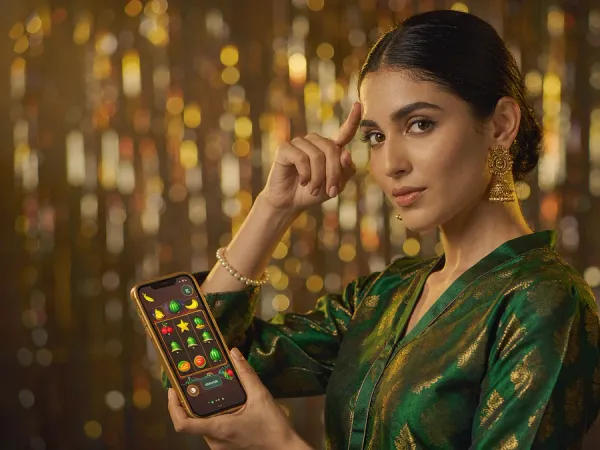 sportsbet.io + Woman in an emerald and gold kameez holding a phone with a glowing slot game